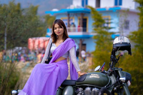 A woman in a purple sari sitting on a motorcycle