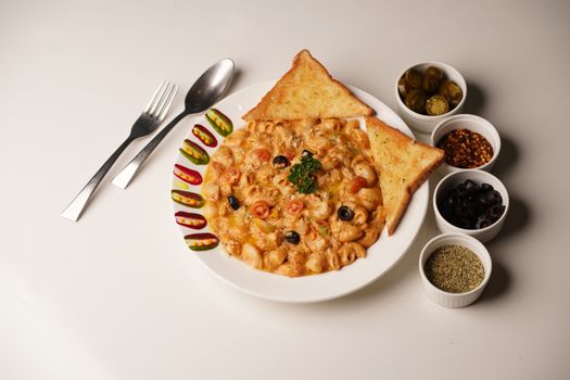 Savor a plate of creamy pasta served with garlic toast, garnished with olives and vibrant spices for a flavorful meal.