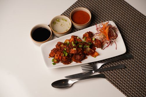 Free Plate of Asian-style crispy chicken with side sauces and garnished vegetables on a dining table. Stock Photo
