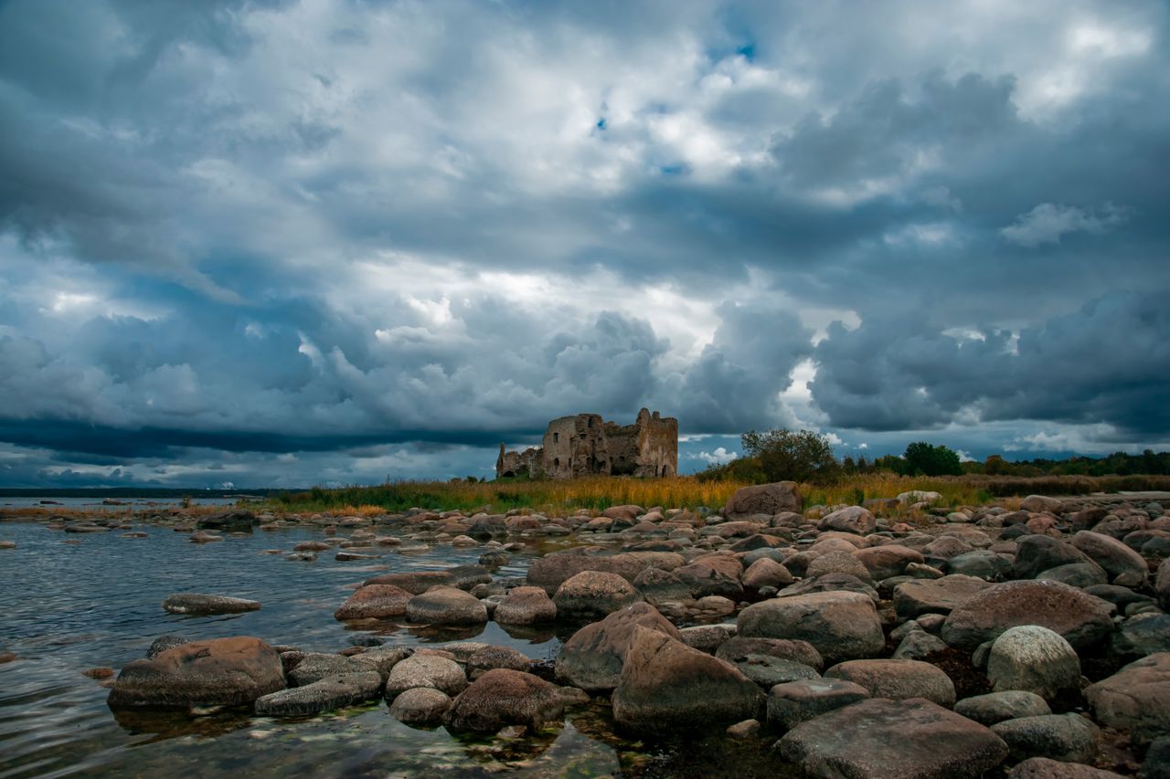 dramatic view of ancient castle ruins by a rocky lake under an overcas
