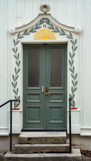 Elegant double doors with olive leaf motifs and sun design above, set on stairs.