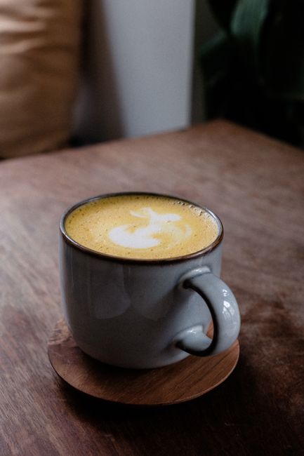 Warm cup of latte with frothy art on a wooden surface, capturing a cozy ambiance.