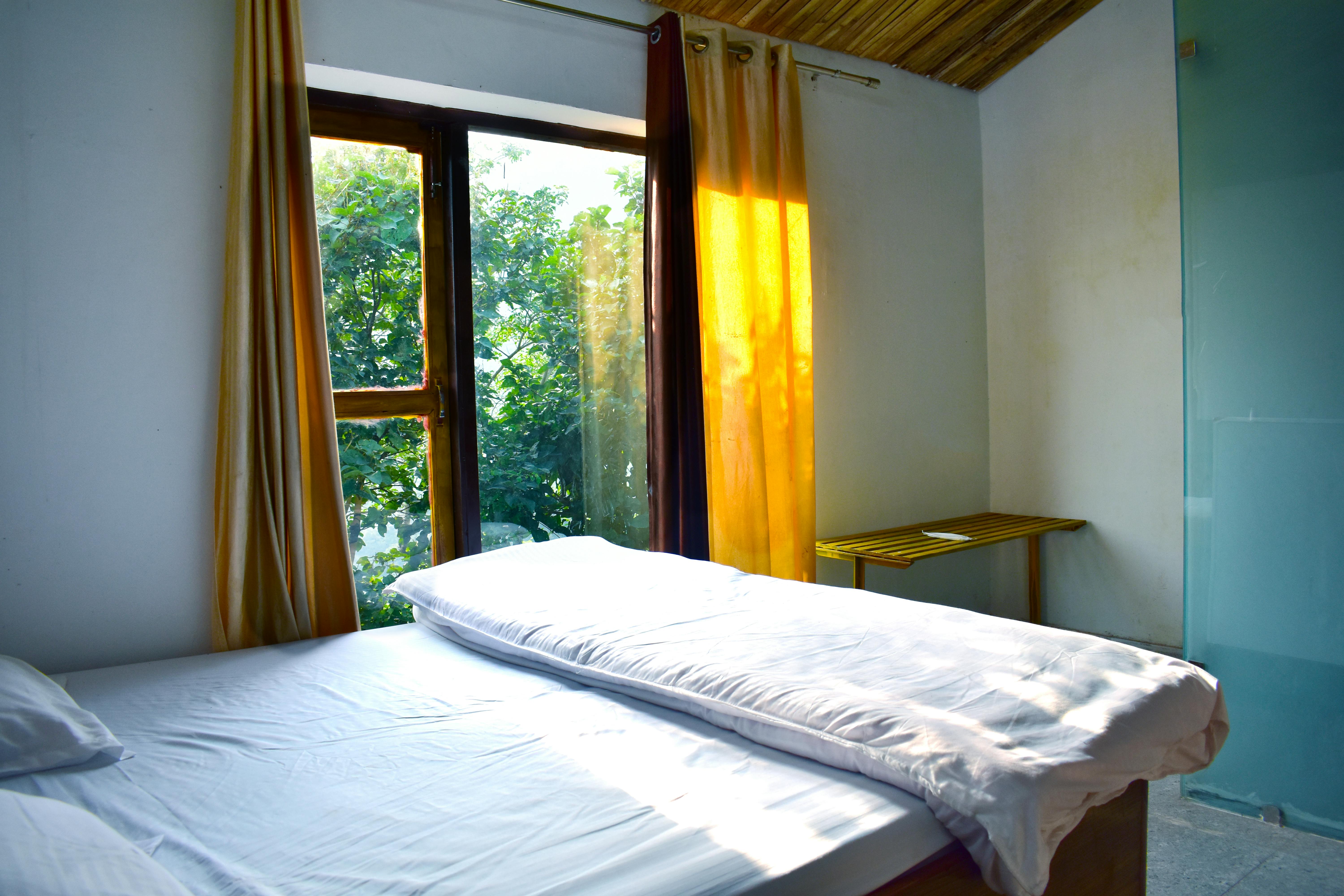 Simple and cozy bedroom interior design with large windows and natural light in Sahibzada Ajit Singh Nagar, India.