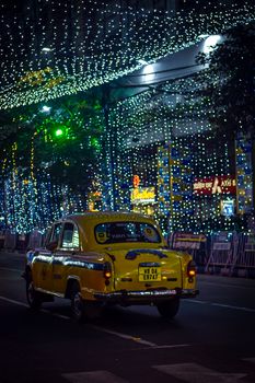 Yellow taxi driving through a city street adorned with festive lights at night.