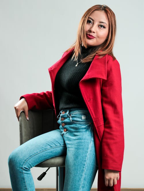 A woman in a red coat and jeans posing for a photo