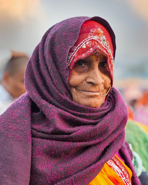 An old woman wearing a purple scarf and a red headscarf