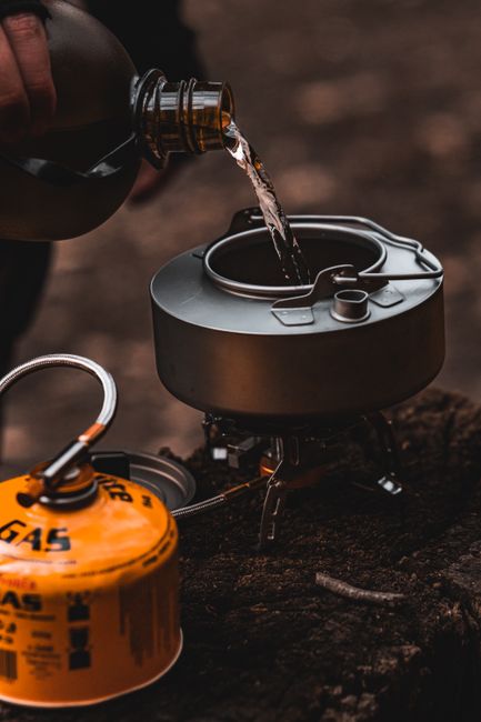 Organized camping gear laid out on a tailgate including tent, backpack, stove, sleeping bag, water bottles, and cookware