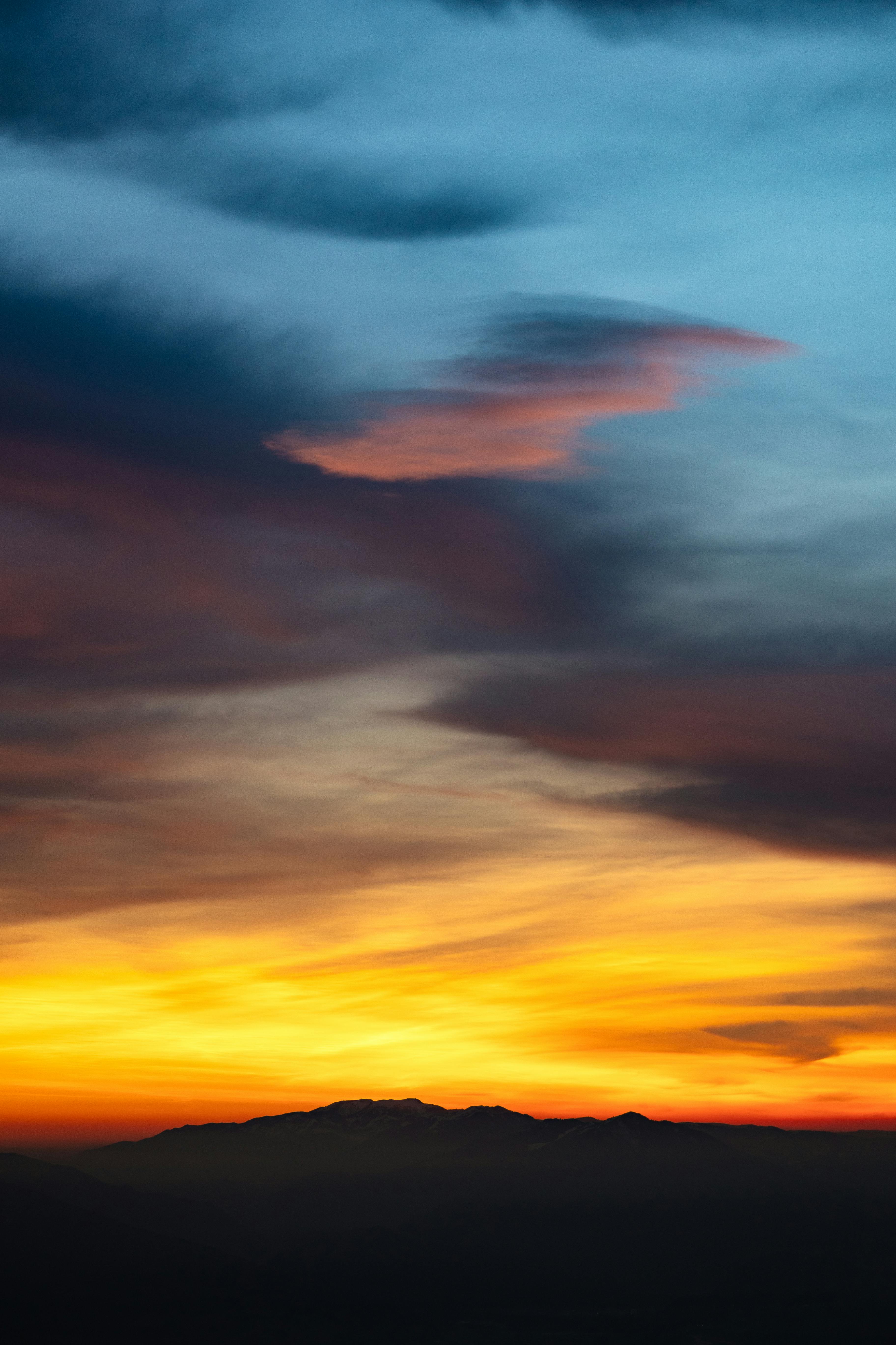 A vibrant sunset over mountains with dramatic clouds and vivid colors.