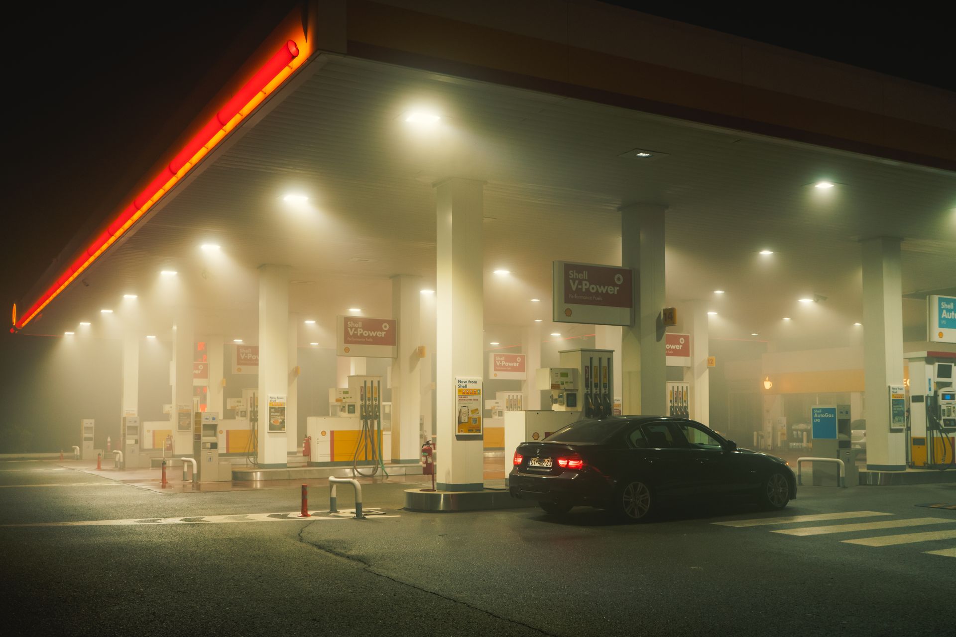 A misty, illuminated gas station at night with a parked sports car under glowing lights.