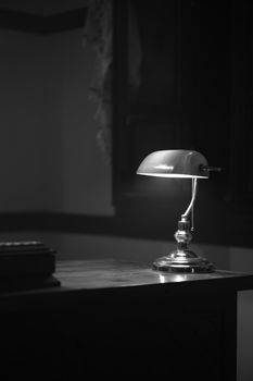 A retro desk lamp casting a soft light in a black and white still life setting.