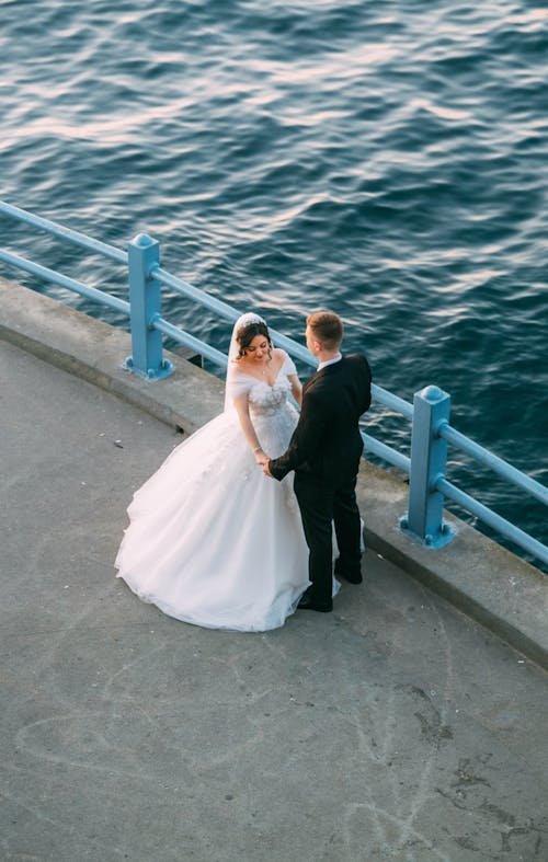 A bride and groom standing on the pier by the water