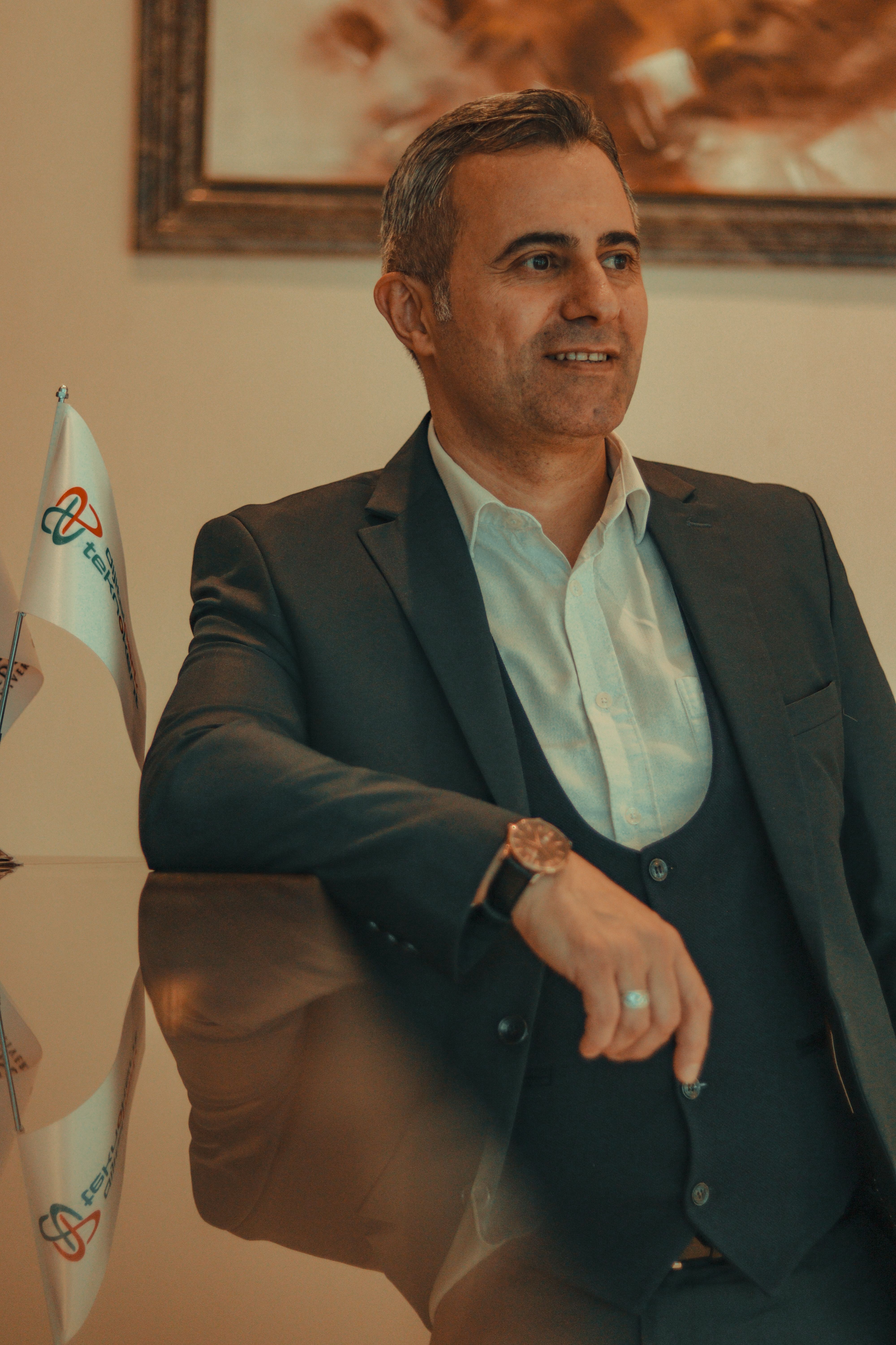 Portrait of a confident businessman in a suit leaning on a glass countertop with a serene expression.