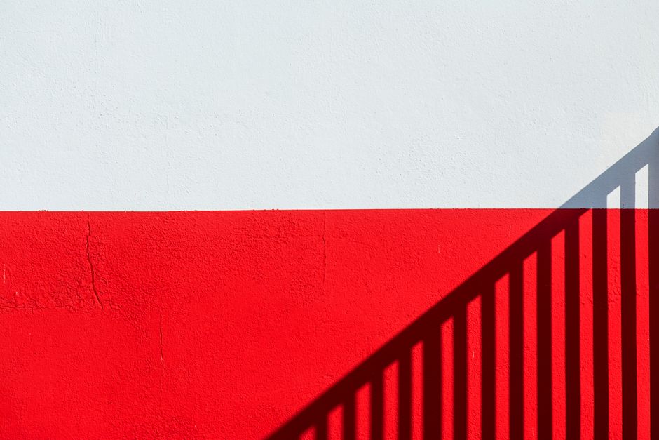 A minimalist photo of a red and white wall with shadows casting a geometric pattern.