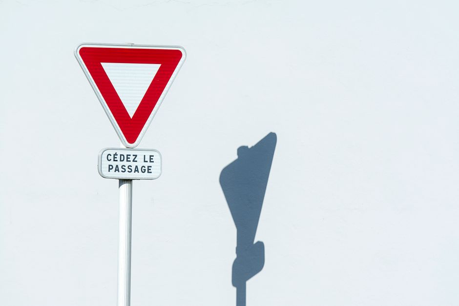 French yield sign 'Cédez le passage' with shadow on white wall backdrop.