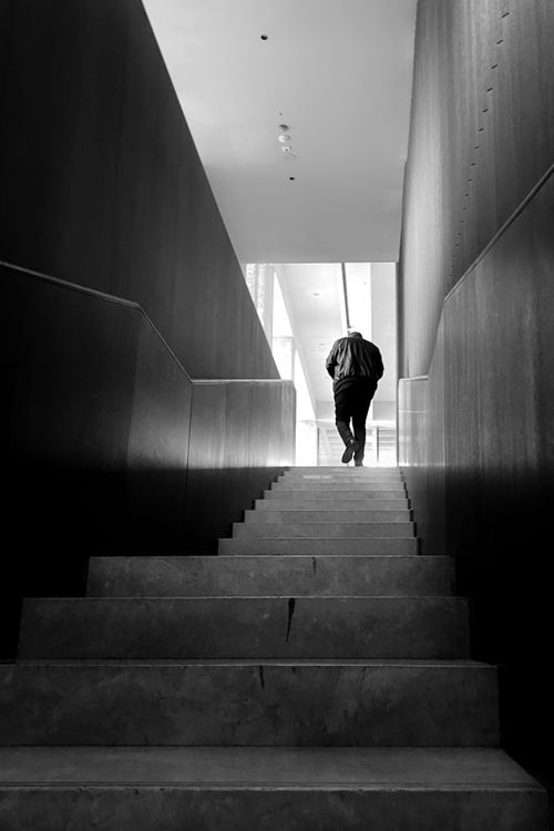 Free A man in a jacket walks upstairs between dark walls in a black and white setting. Stock Photo