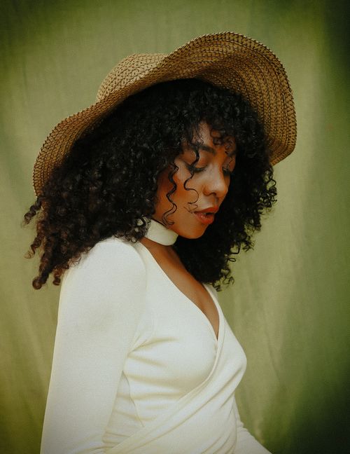Free Elegant portrait of a woman with curly hair wearing a fashionable hat, looking downward. Stock Photo
