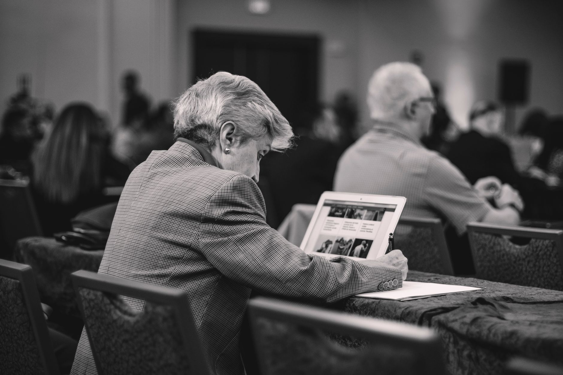 A senior journalist takes notes during a conference, engrossed in thought.