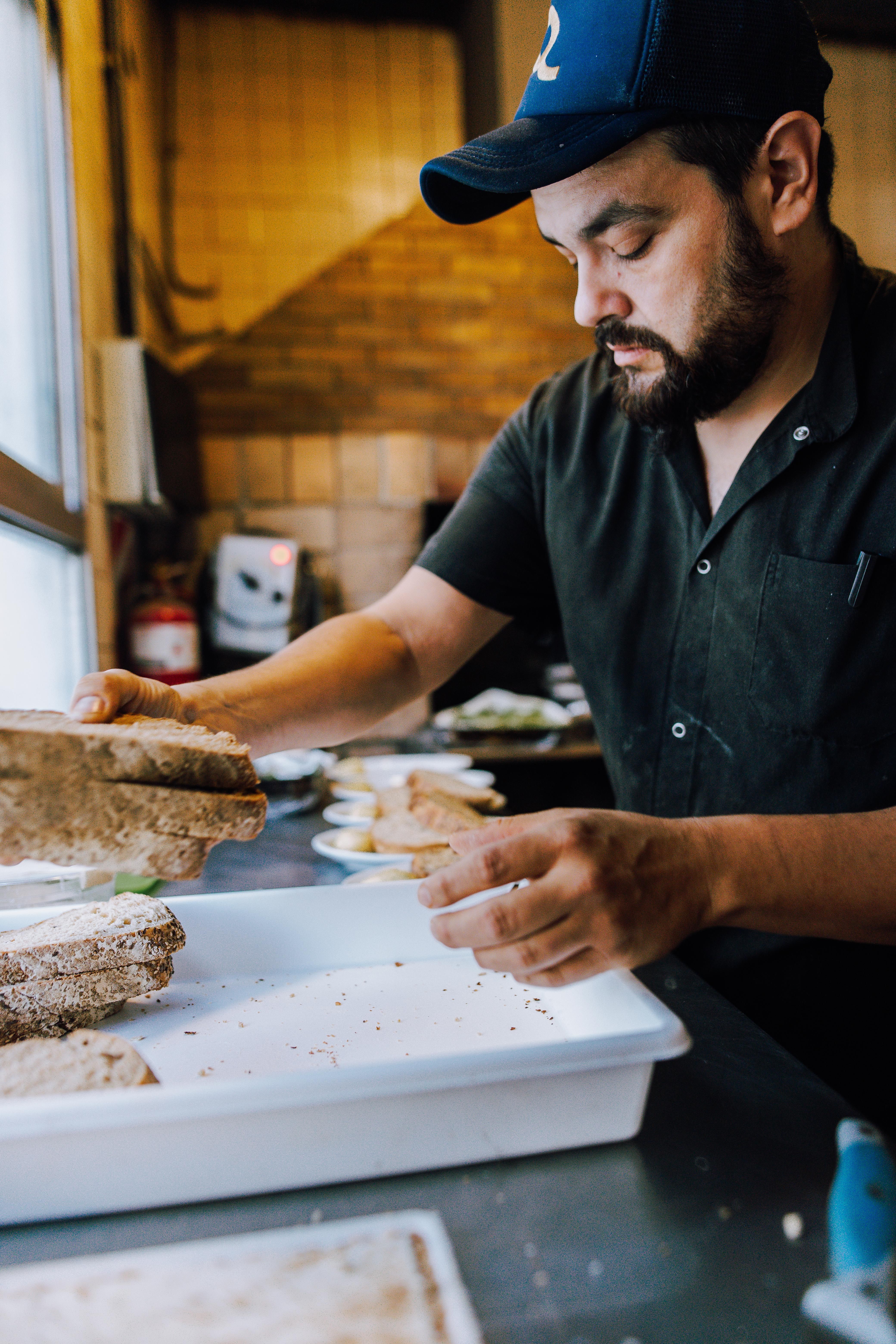 Chef wearing a cap assembling sandwiches in a Buenos Aires kitchen, captured in a moment of concentration.