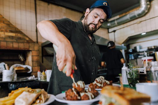 A chef in Buenos Aires attentively garnishes plates with sauce in a bustling kitchen.