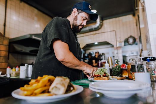 Chef skillfully prepares a sandwich in a vibrant Buenos Aires kitchen setting.