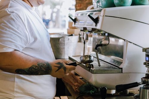 Free Barista making coffee with espresso machine in Buenos Aires café. Close-up of tattooed arm and coffee preparation. Stock Photo