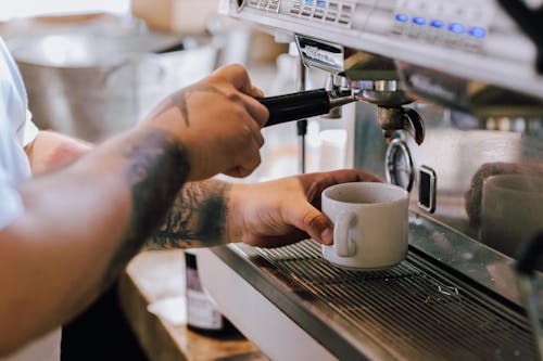 Man Arms with Tattoos Holding Cup and Using Coffee Machine