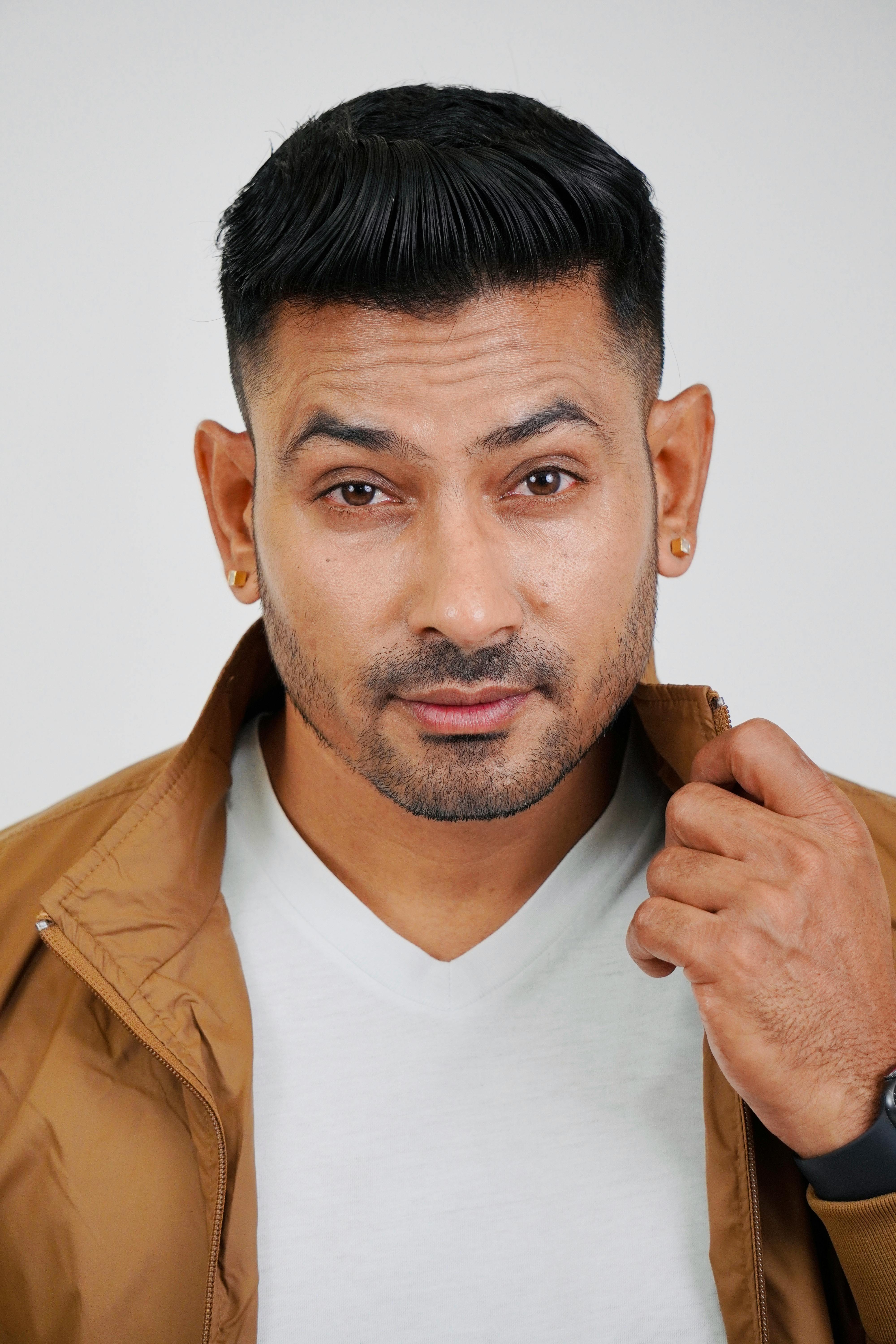 Studio portrait of a man in a brown jacket with vibrant expression on a white background.