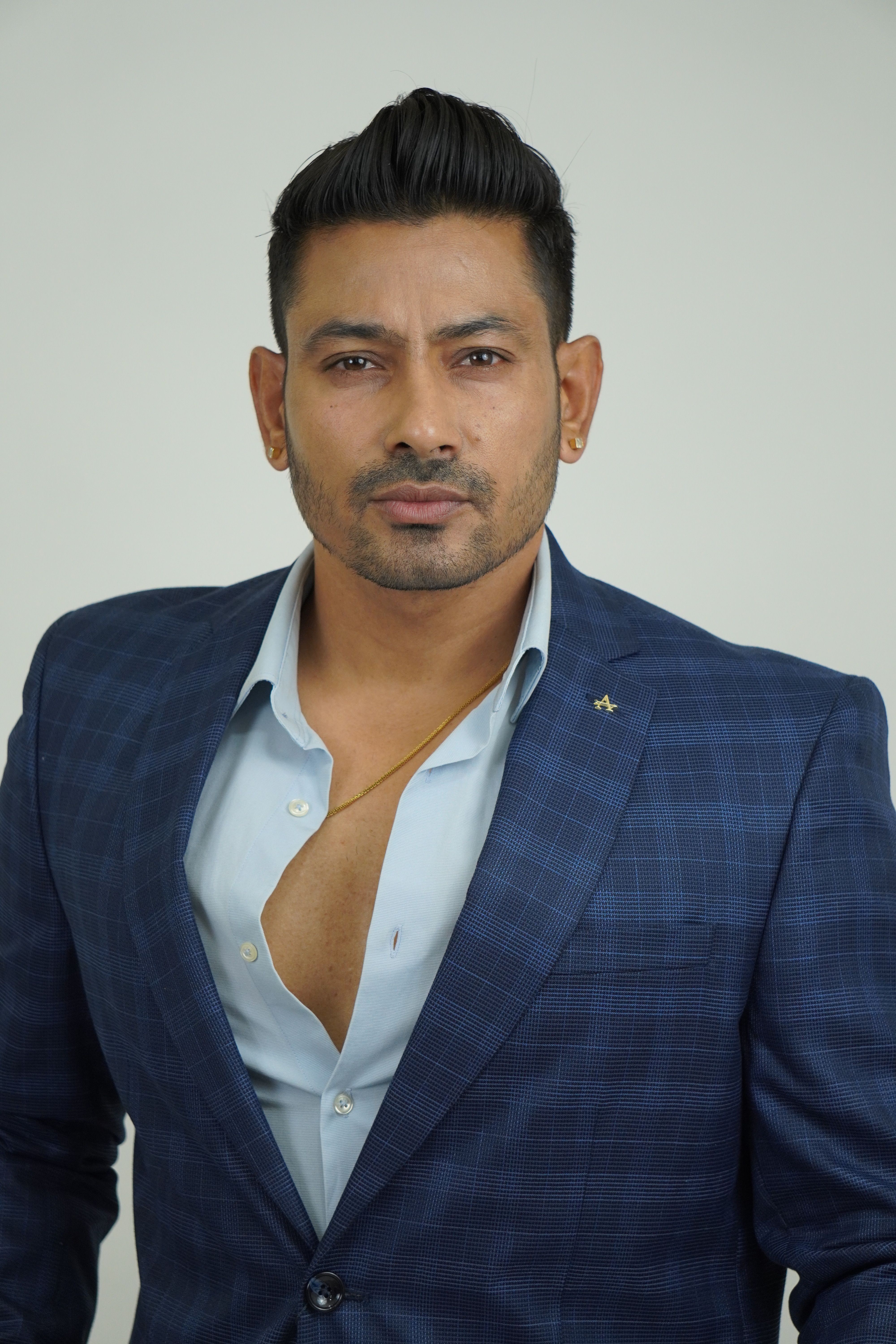 A stylish businessman posing confidently in a blue suit in a studio setting.