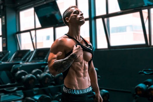 Muscular man showing abs and tattoos in a gym setting.