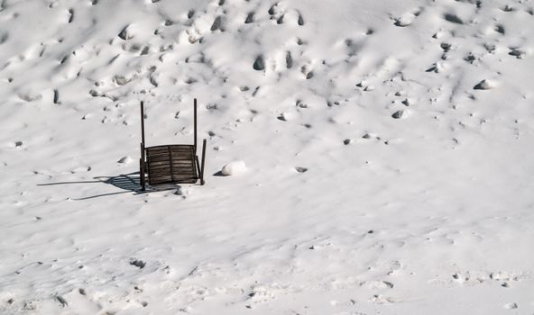 An upside down wooden chair casting shadows on snowy ground in winter.