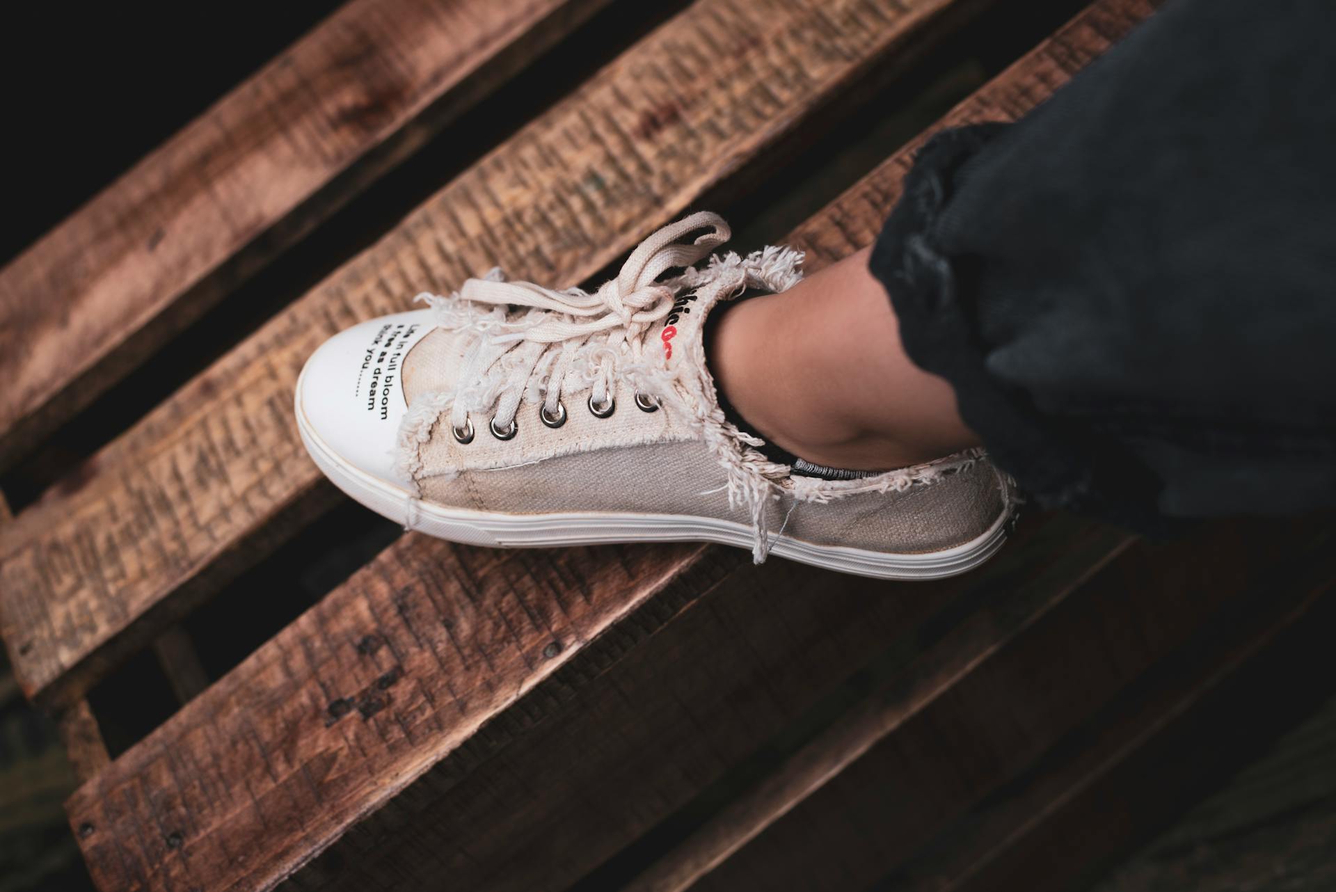 Frayed beige sneaker on wooden pallet evokes rustic urban style.
