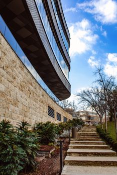 A modern architectural facade with glass and stone elements, featuring outdoor stairs and landscaped greenery in Ankara, Türkiye.