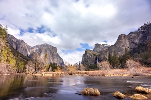 Free Stunning view of Yosemite Valley featuring majestic cliffs, trees, and waterfalls under a cloudy sky. Stock Photo