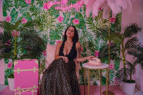 Free Elegant woman posing in a vibrant room with tropical decor and neon sign. Stock Photo