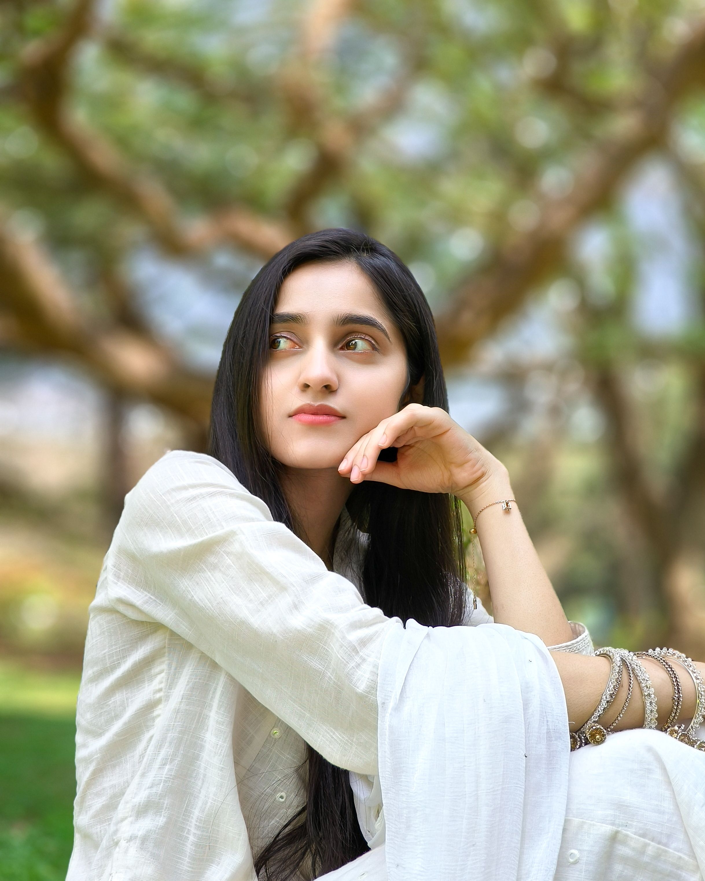 A thoughtful young woman in a white outfit poses in a beautiful Bengaluru park.