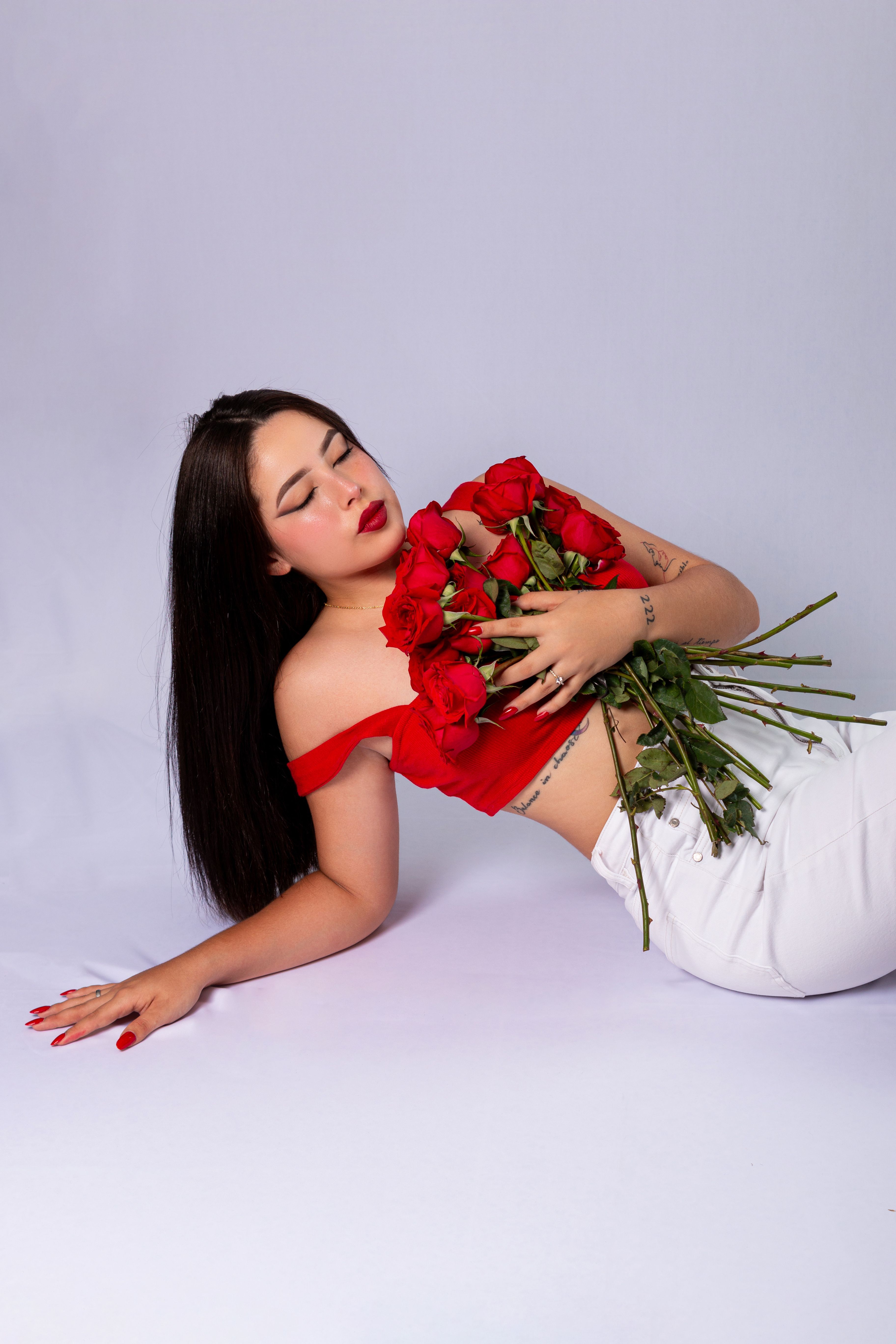 A woman in red and white attire poses gracefully holding red roses, symbolizing elegance and romance.