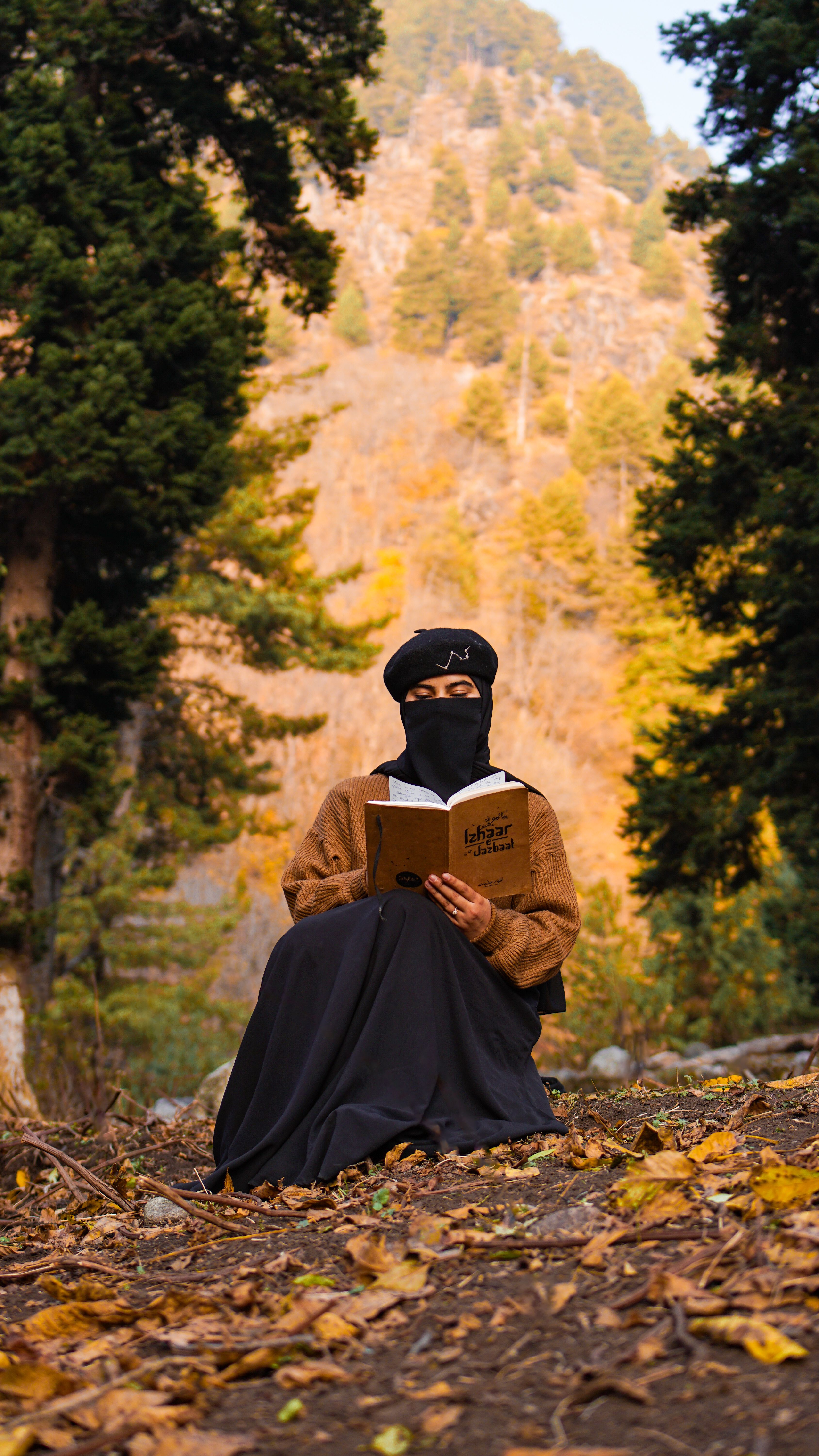 A man in traditional attire reads a book amidst an autumn forest landscape.
