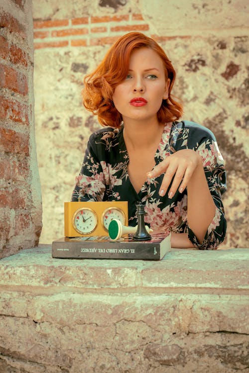 A woman with red hair sitting on a ledge with a clock