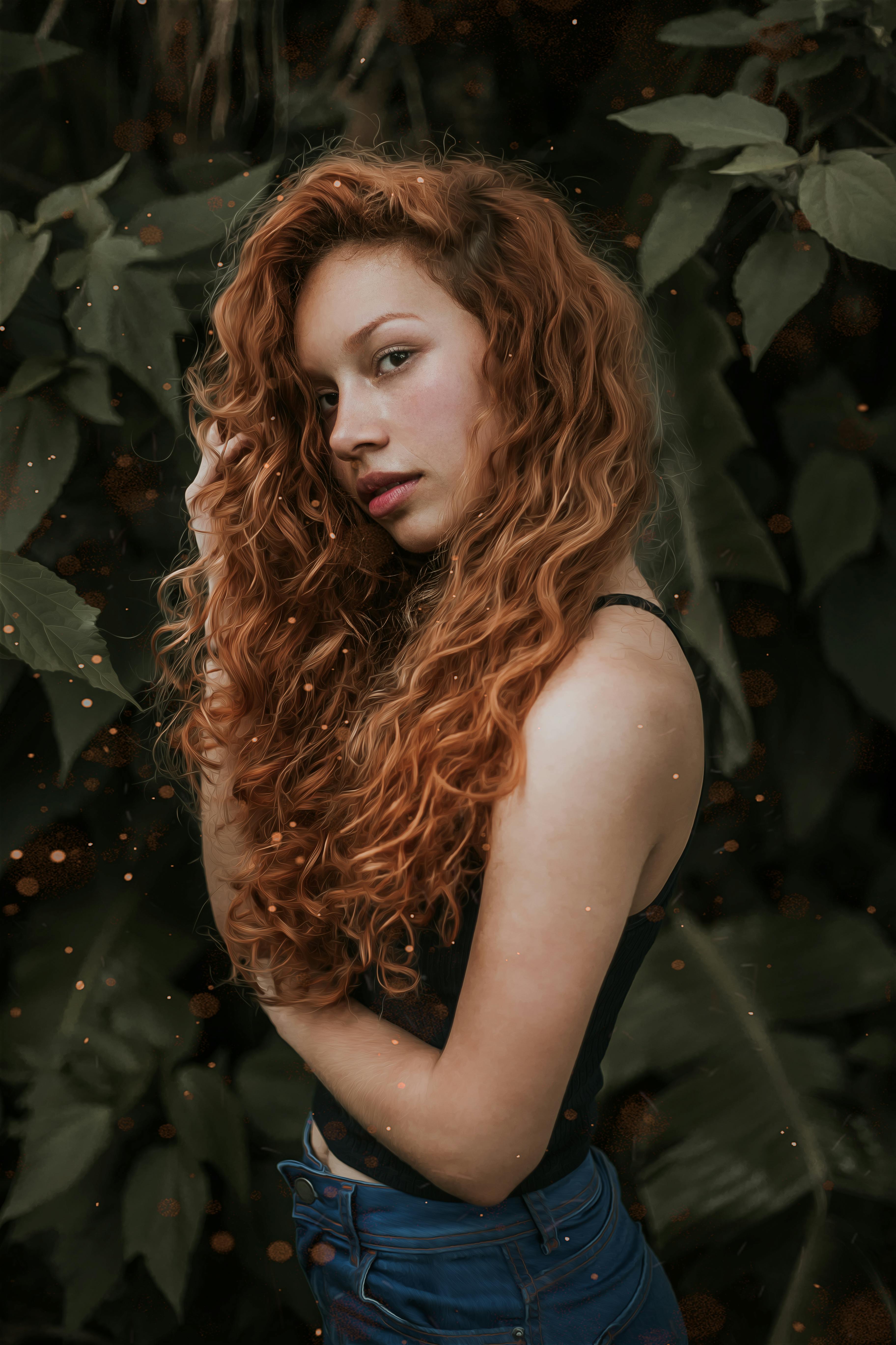 一位红发卷曲的美丽年轻女子在郁郁葱葱的绿叶前摆姿势