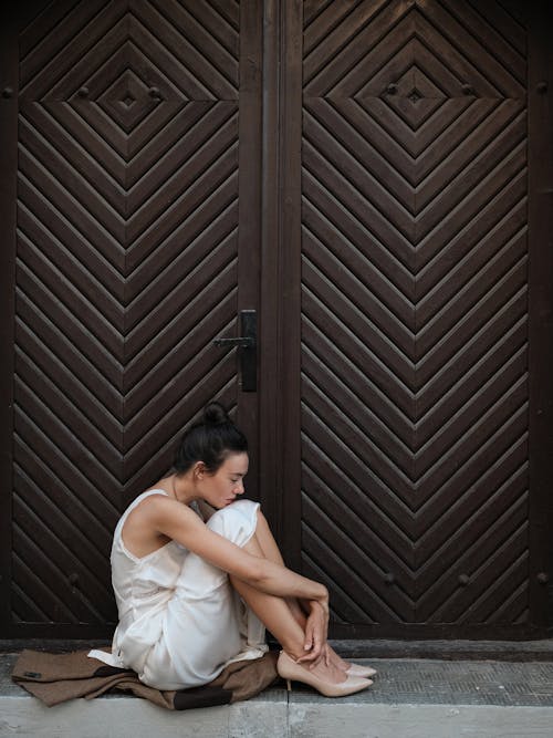 A woman sitting on the ground in front of a wooden door