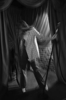Blurred image of a woman on stage during a rehearsal with a microphone and curtain backdrop.