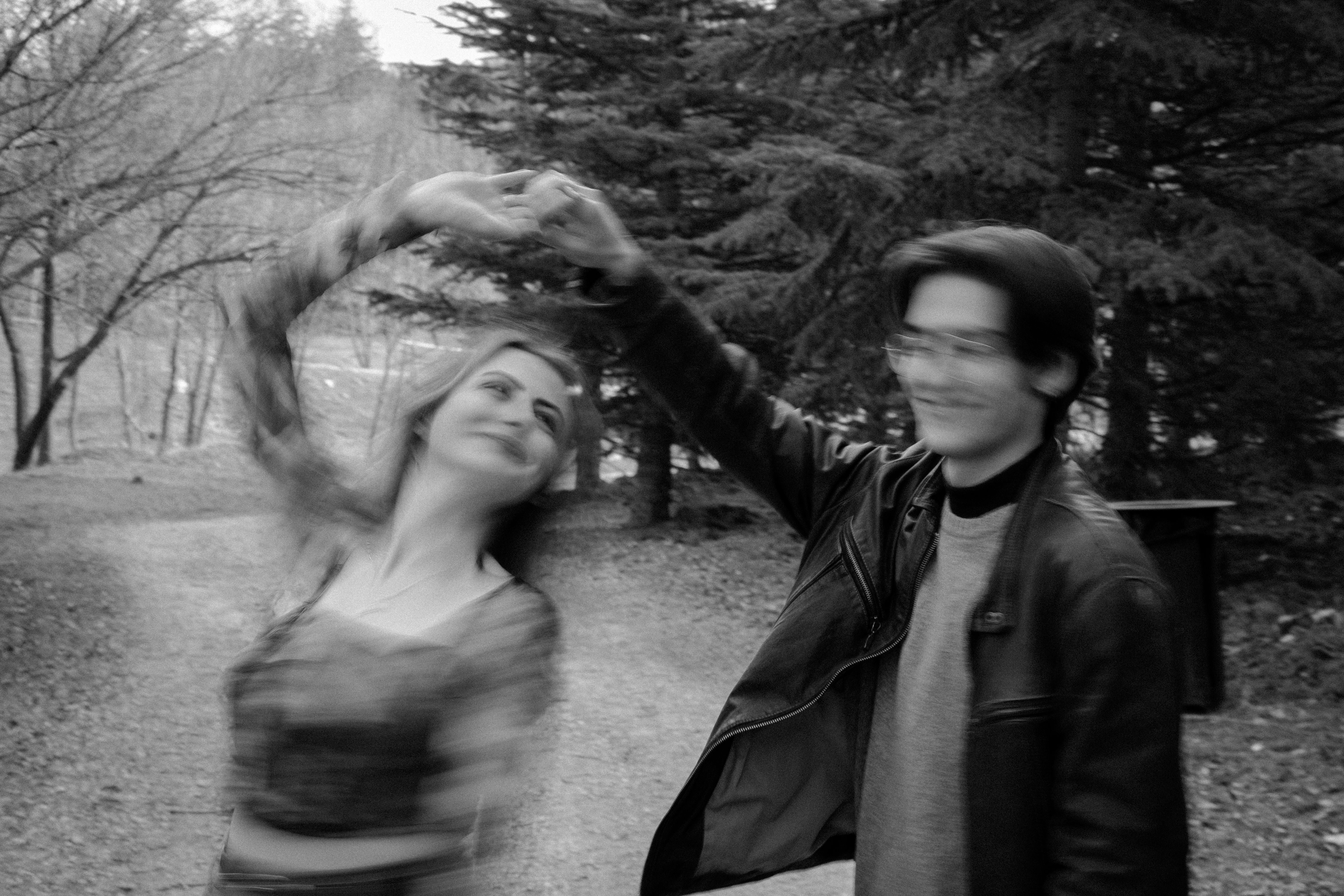 A joyful couple dances on a forest path with blurred motion. Black and white.