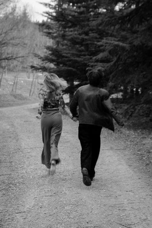 A black and white photo of a man and woman running down a dirt road
