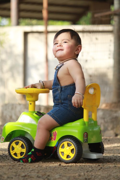 Smiling baby boy sitting on a green toy car outdoors