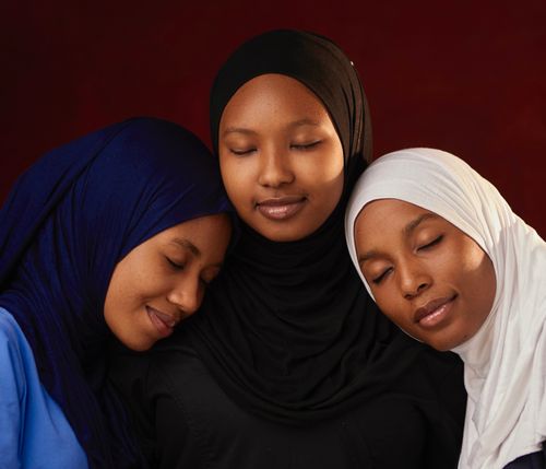 Free A harmonious portrait of three women wearing hijabs with eyes closed, against a warm backdrop. Stock Photo