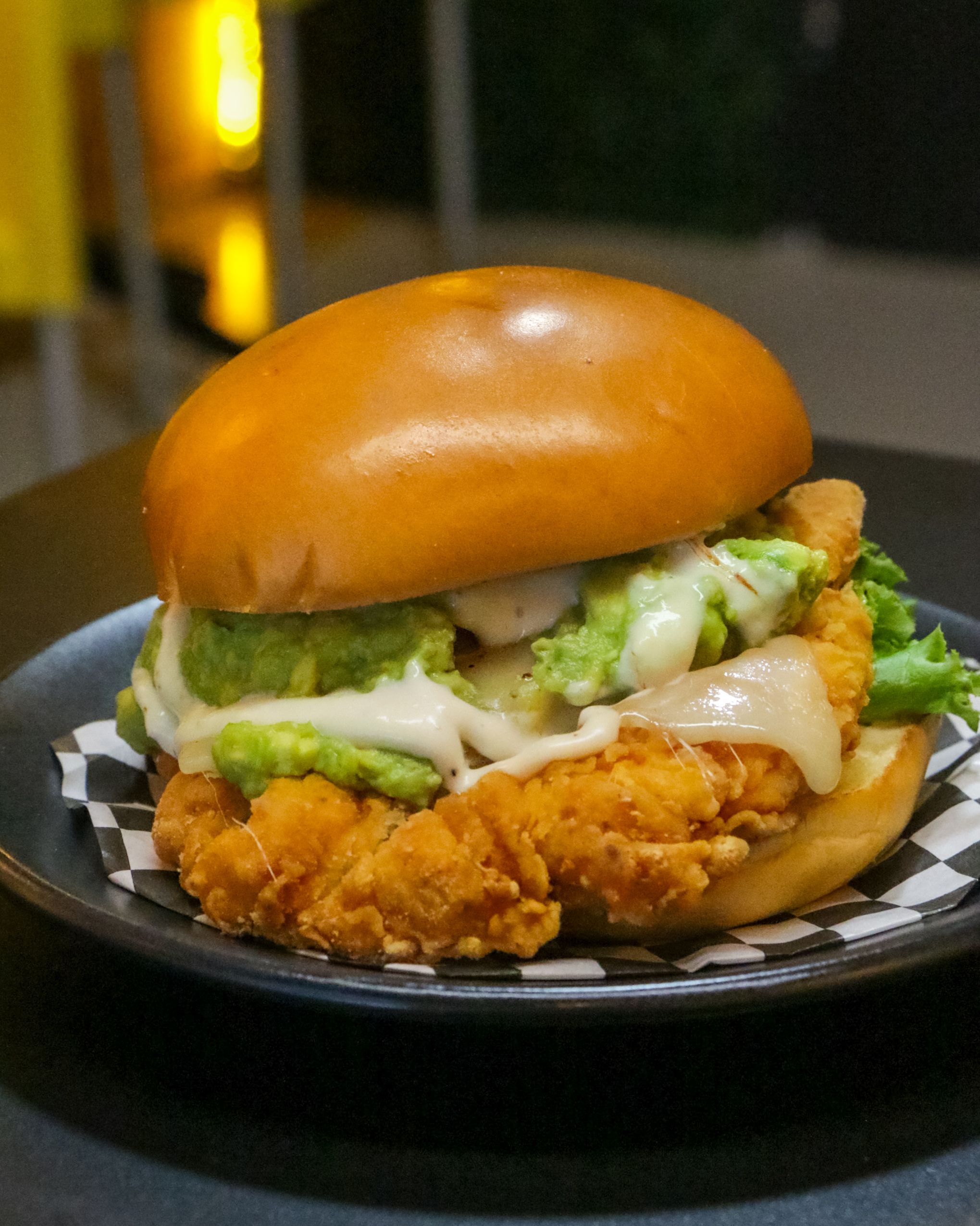 Anya  Juárez Tenorio - Tasty fried chicken burger with lettuce and cheese served on a stylish black plate.