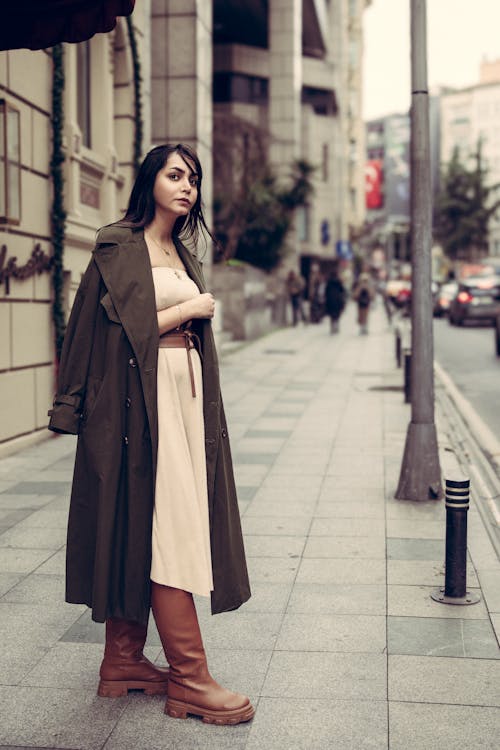 A Fashionable Woman in a Dress and Trench Coat Standing on a Sidewalk 