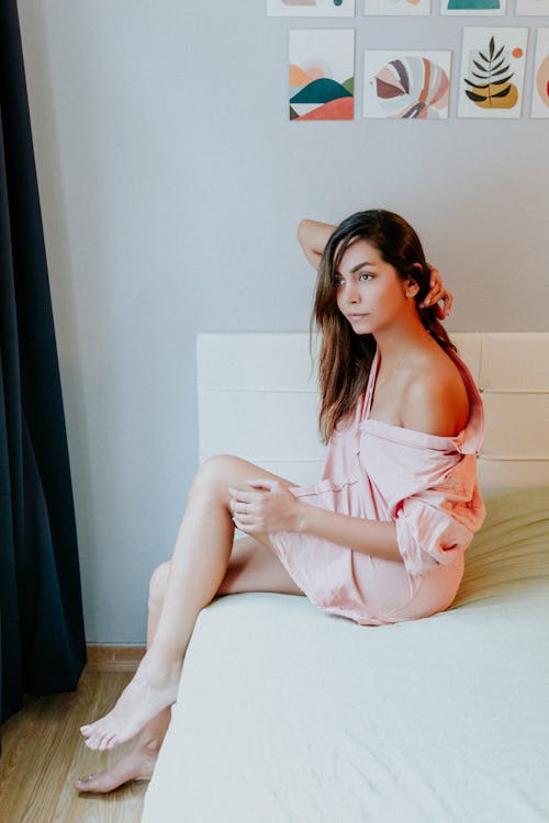 Young Woman in a Pink Shirt Sitting on a Bed 