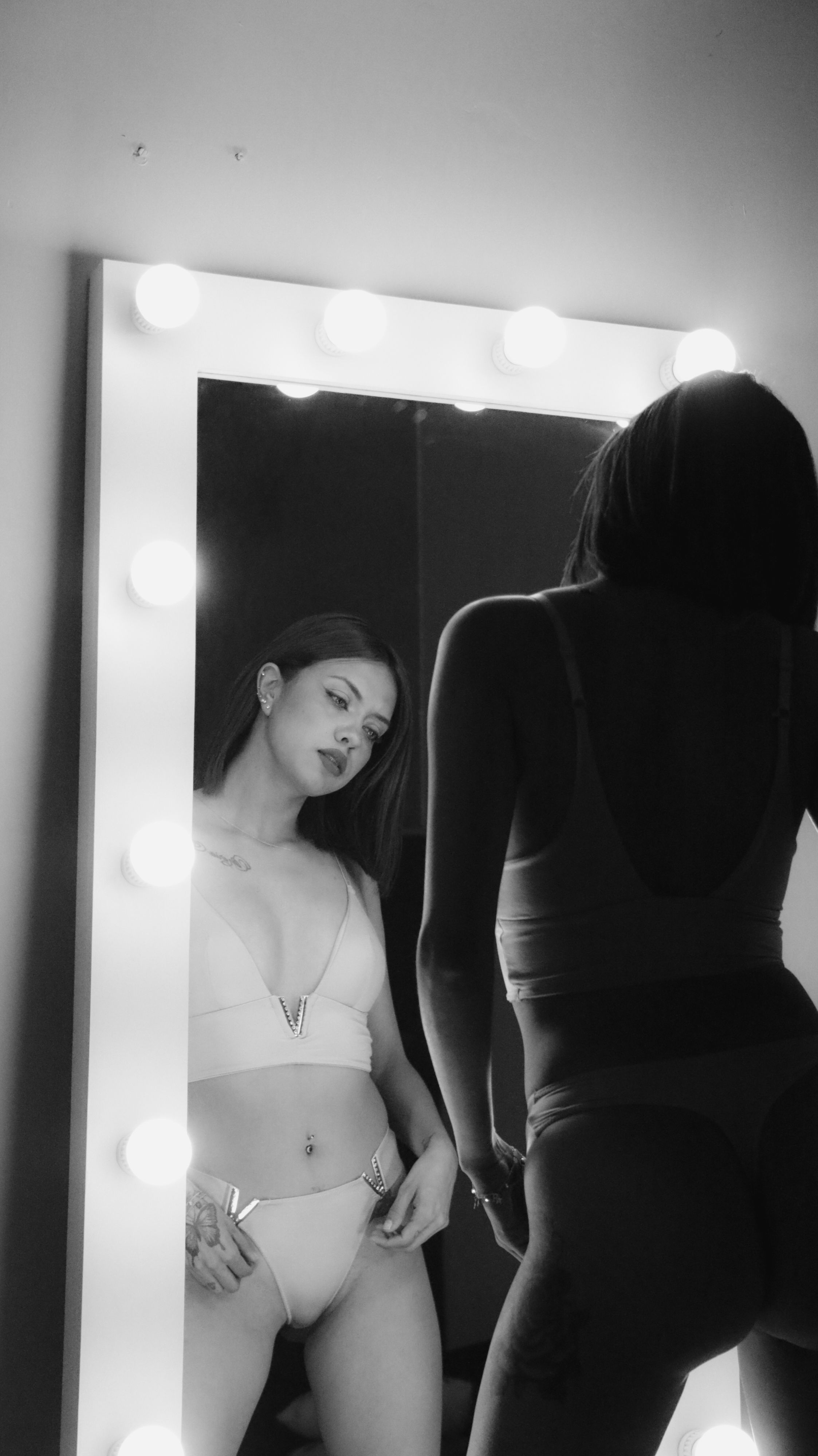 Elegant black and white photo of a woman in lingerie looking into a mirror.