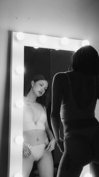 Elegant black and white photo of a woman in lingerie looking into a mirror.